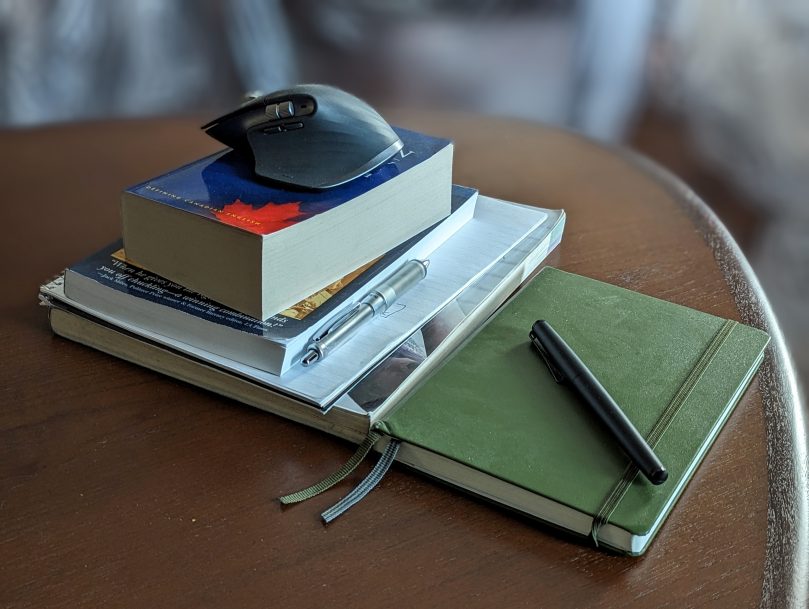 A pile of course materials and notebooks with a computer mouse sitting on top.